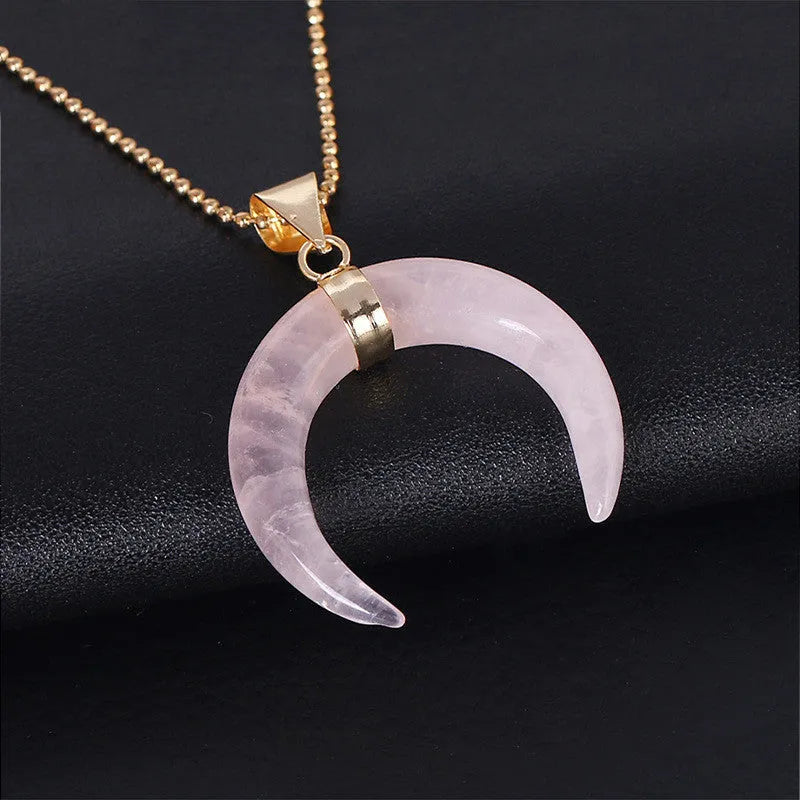 Close-up of a moon pendant necklace with a pink natural stone, on a copper-coloured chain against a neutral background.