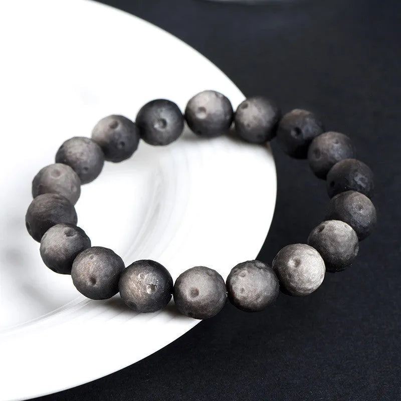 Natural obsidian crater ball bracelet with meteorite-like texture in silver stone or gold finish.
