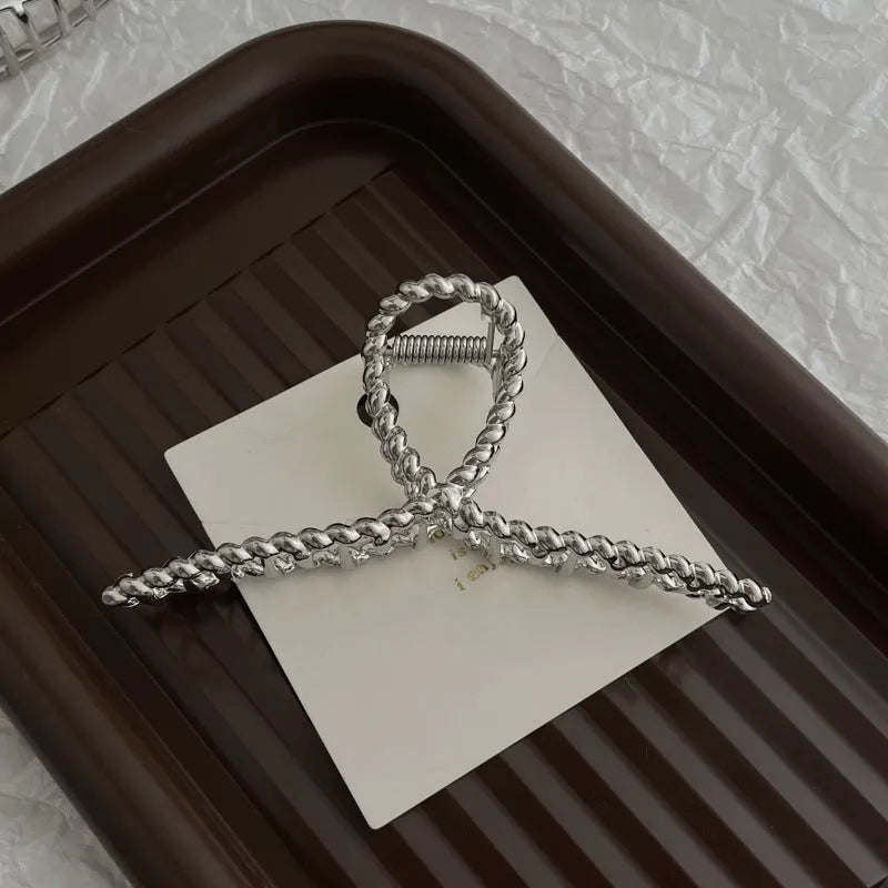 Assorted silver metal hair claws and barrettes including wave, knot, bow, and pearl designs on a white background.