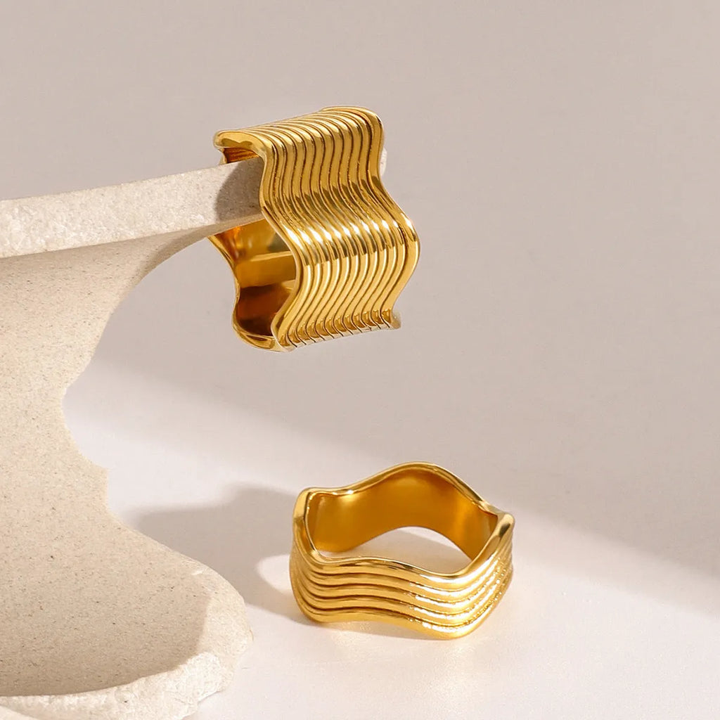 Close-up of a stainless steel ring with a wide geometric wave pattern and electroplated metallic finish.