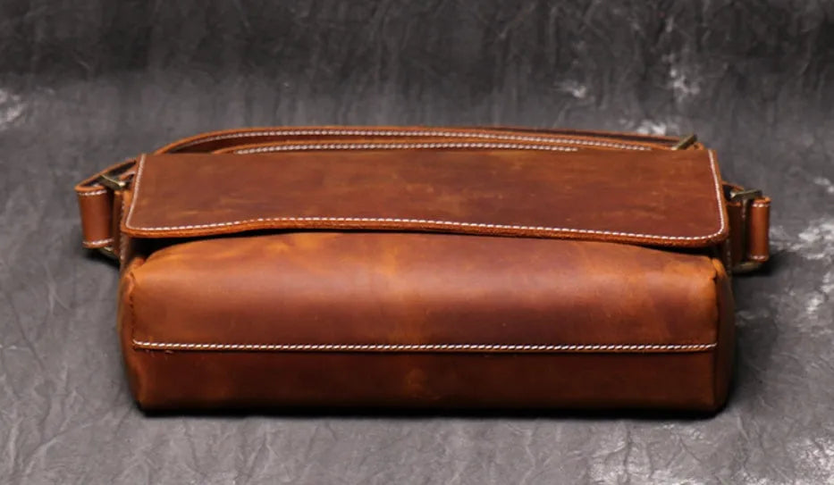 Men's vintage brown leather messenger bag with adjustable strap, shown open to reveal internal organiser pockets.