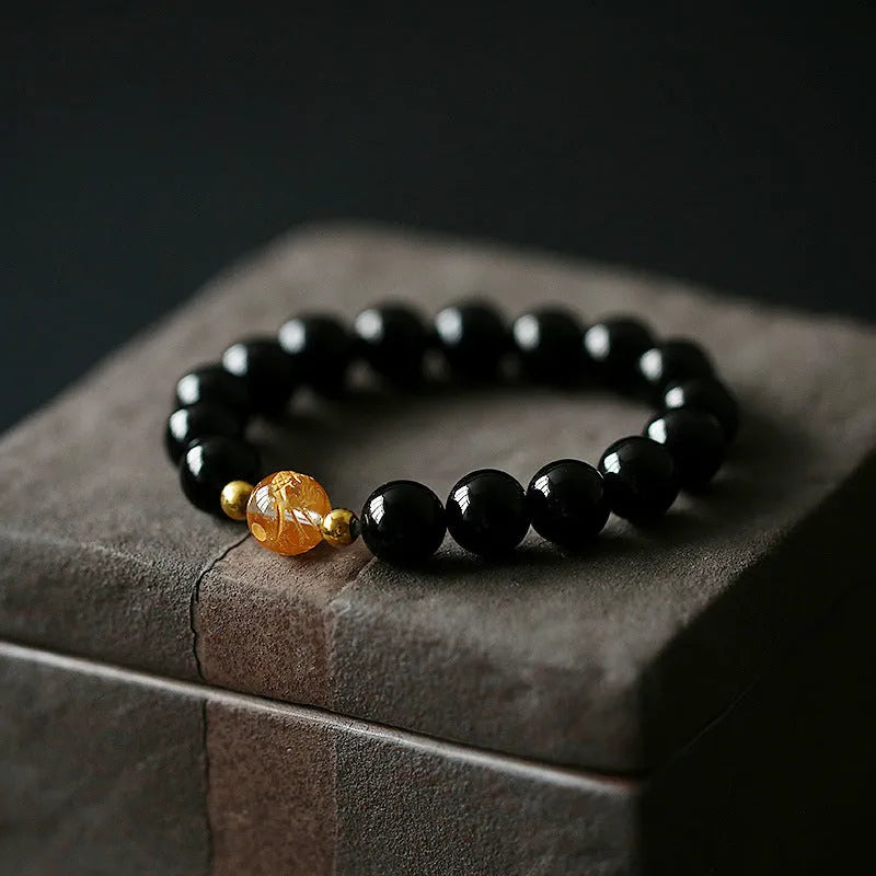 Geometric obsidian and white crystal beaded bracelet with golden dragon charm on a wrist.