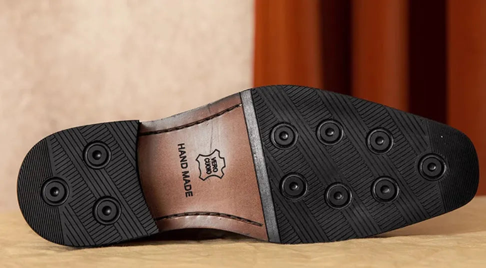 Men's black leather slip-on loafers with fringe detailing on a wooden floor