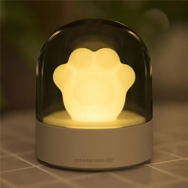 Grey or pink cat paw shaped USB rechargeable night light and music box on a desktop.