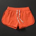 Man wearing loose orange red polyester beach shorts with elasticated waistband.