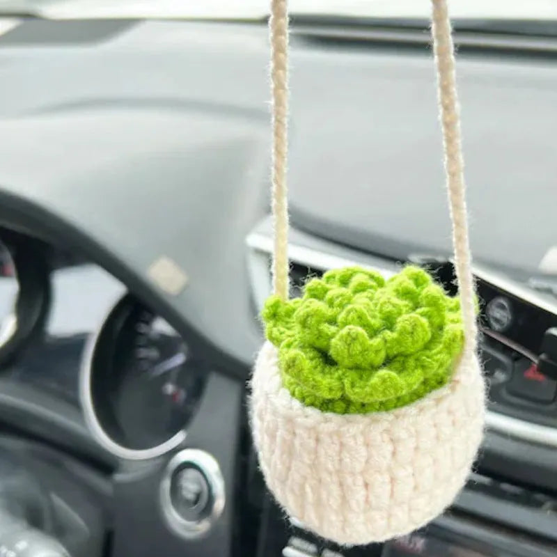 Green and white knitted wool car plant decoration with macramé texture and a white hanging rope.