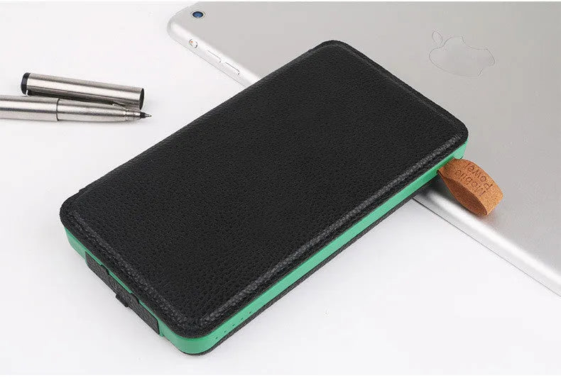Black solar power bank with a solar panel, showing its USB ports and LED light, placed outdoors on a rock.