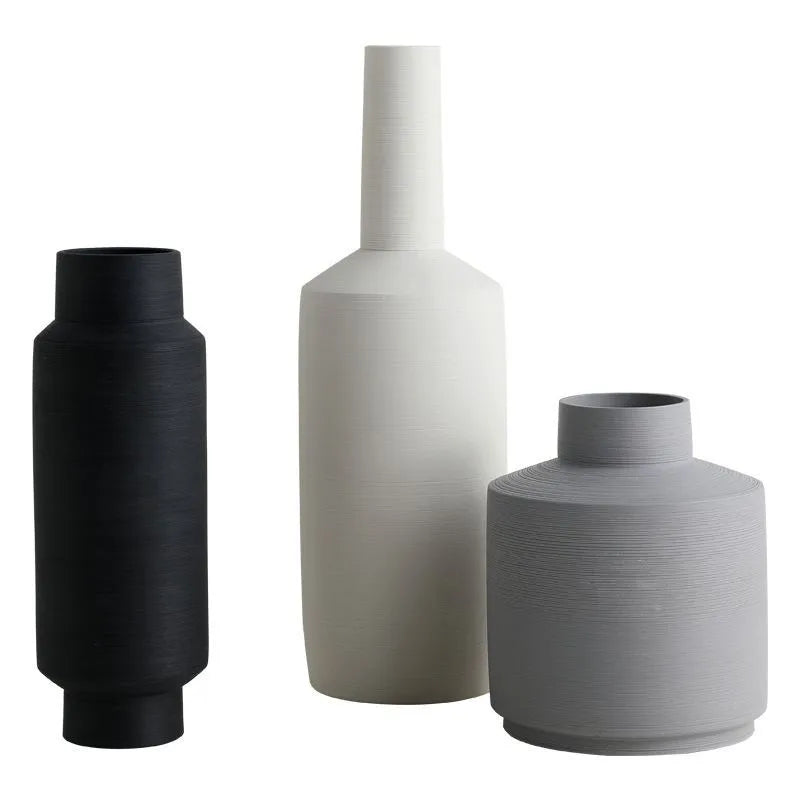 Three Nordic style ceramic vases with wire-drawn finish in neutral gray, black, and ivory white on a wooden table.