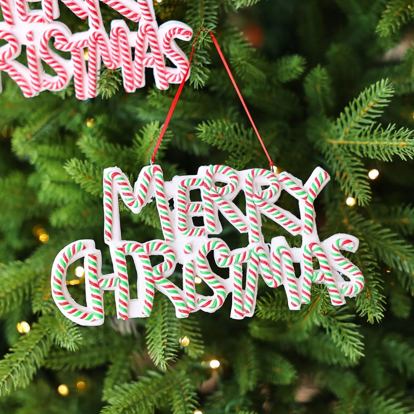Merry Christmas letter plate polymer clay tree ornament in red, white and green plastic hanging on a tree branch