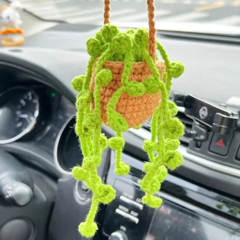 Green and white knitted wool car plant decoration with macramé texture and a white hanging rope.