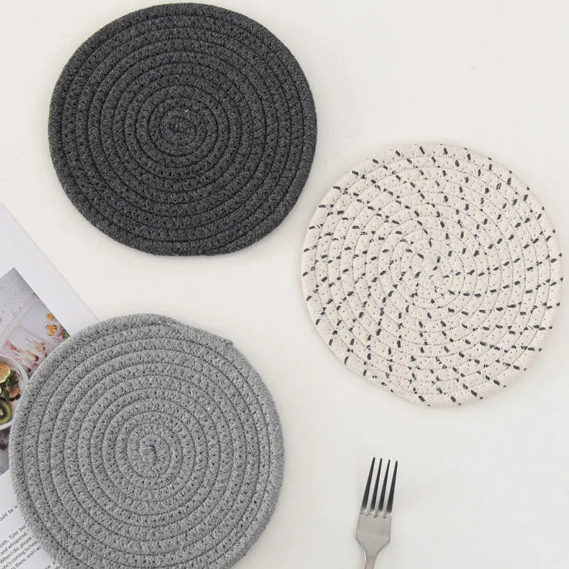 Set of three round grey cotton cord coasters on a wooden table.