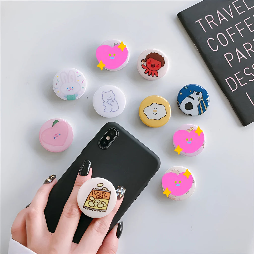 Creative telescopic glue cartoon phone airbag bracket in colour C1 girl design on a desk holding a smartphone