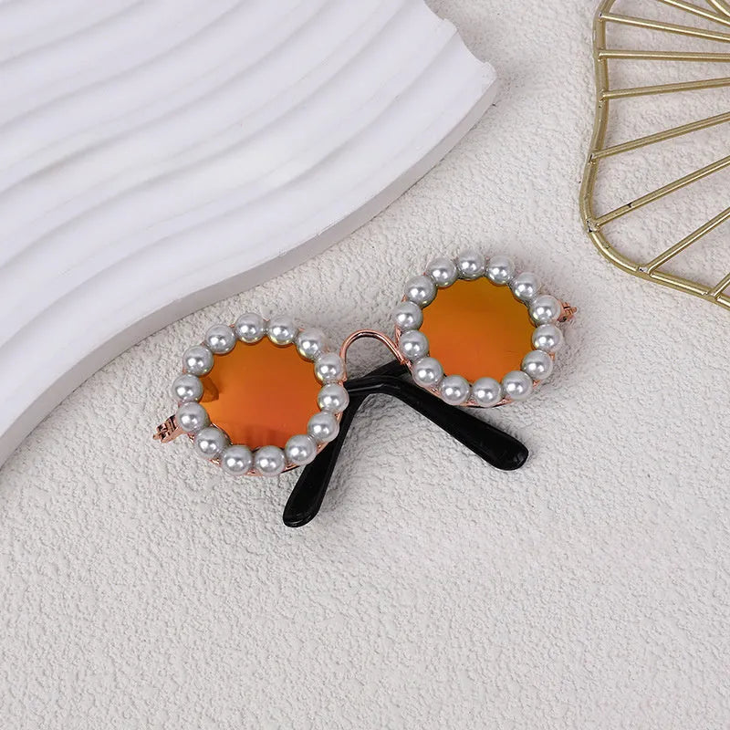 Pearl-rimmed round sunglasses for cats and dogs in multiple colours on a pink background.