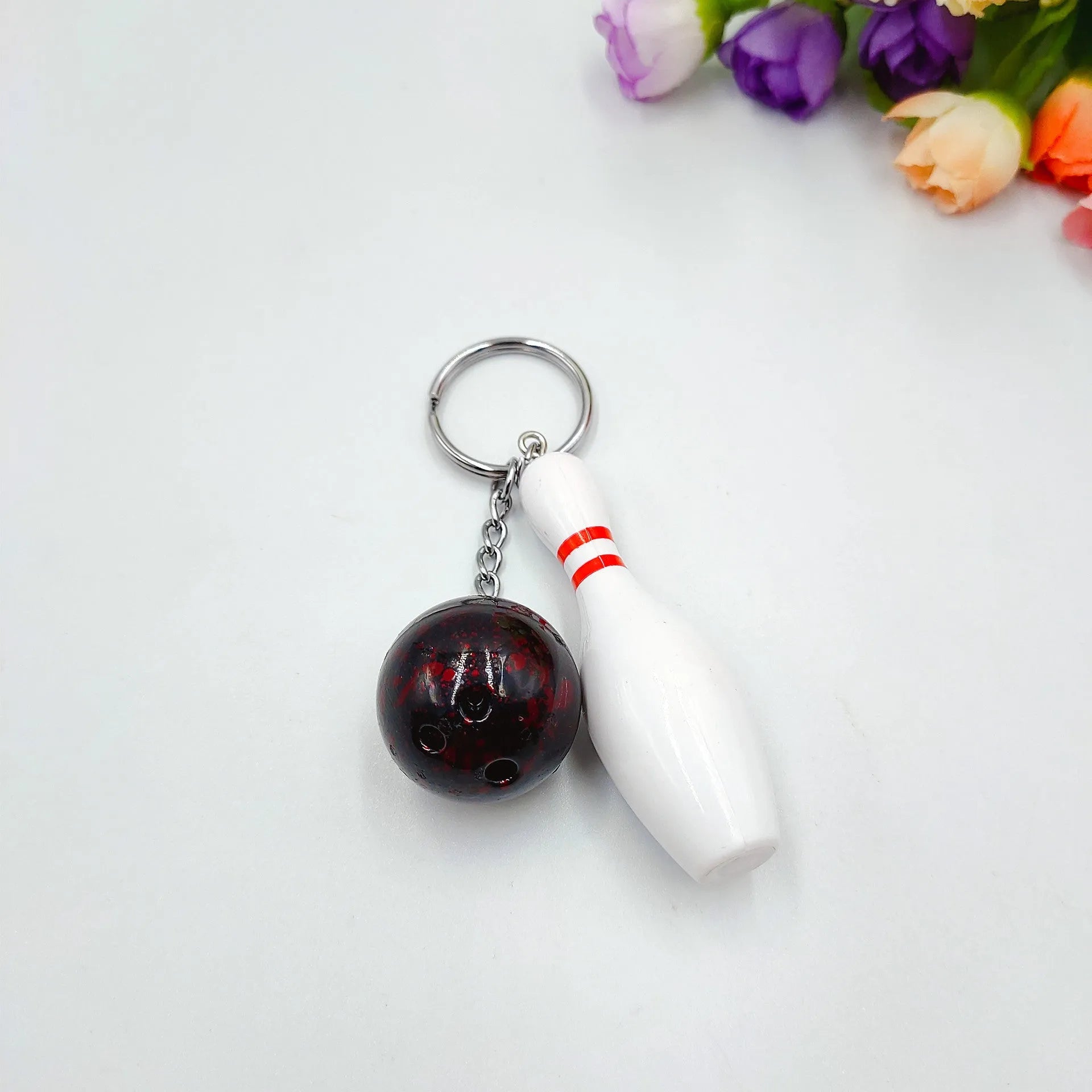 Miniature dark red bowling ball keychain on a metal key ring against a white background.