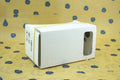 Pink and white cardboard VR glasses for smartphones, shown with 3D lenses and a rubber headband.
