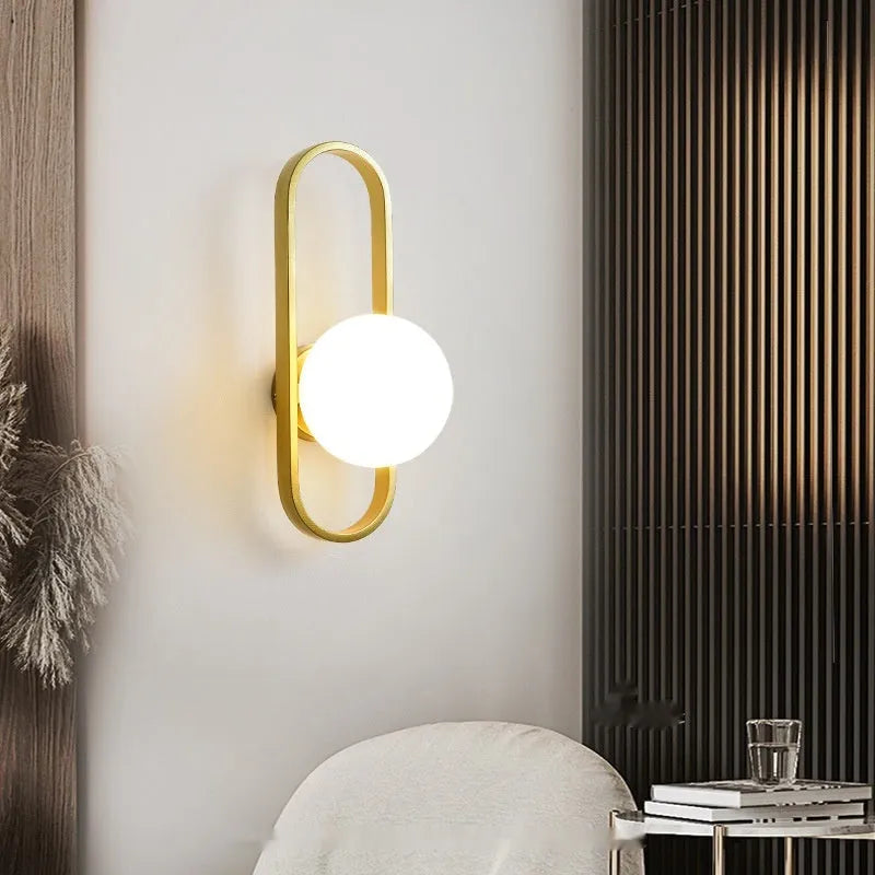 Minimalist modern wall lamp with a clear glass shade on an iron body, shown in a black finish mounted on a wall.