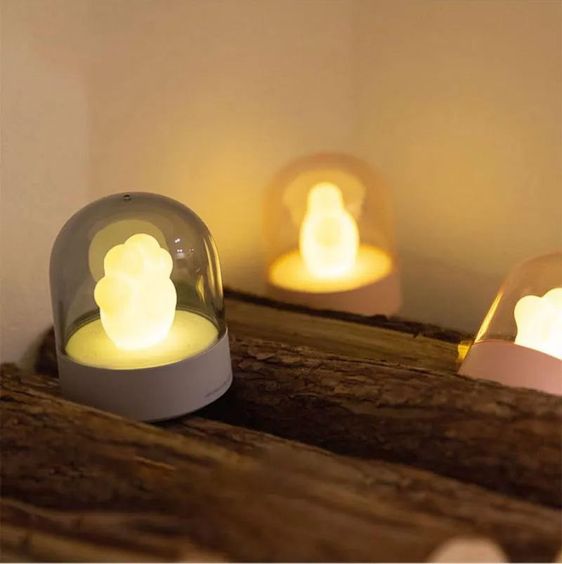 Grey or pink cat paw shaped USB rechargeable night light and music box on a desktop.
