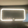 White car sun visor with LED make-up mirror showing illuminated reflection on aluminium surface
