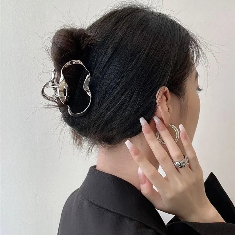 Assorted silver metal hair claws and barrettes including wave, knot, bow, and pearl designs on a white background.