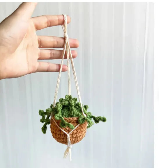 Green and white knitted wool car plant decoration with macramé texture and a white hanging rope.
