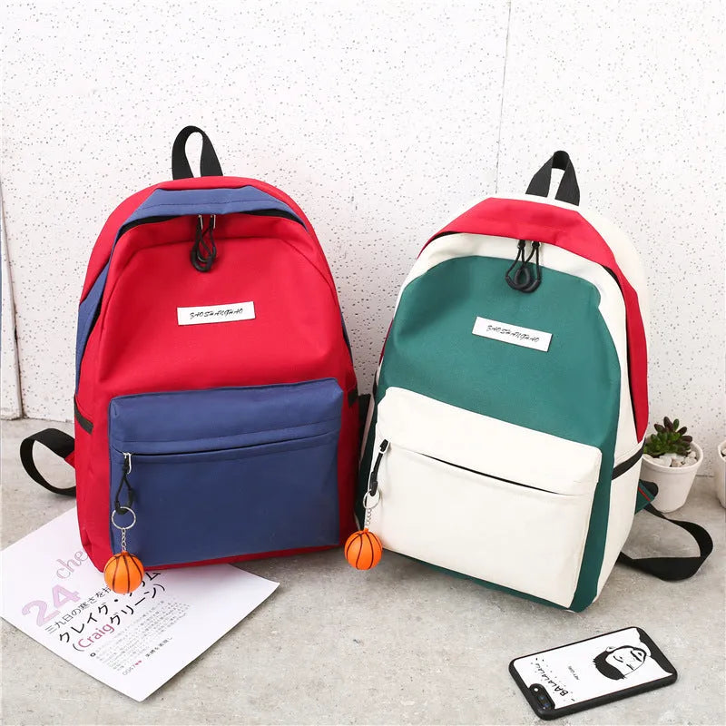 Four medium canvas backpacks in black, green, red, and white with zipper closure and air cushion straps