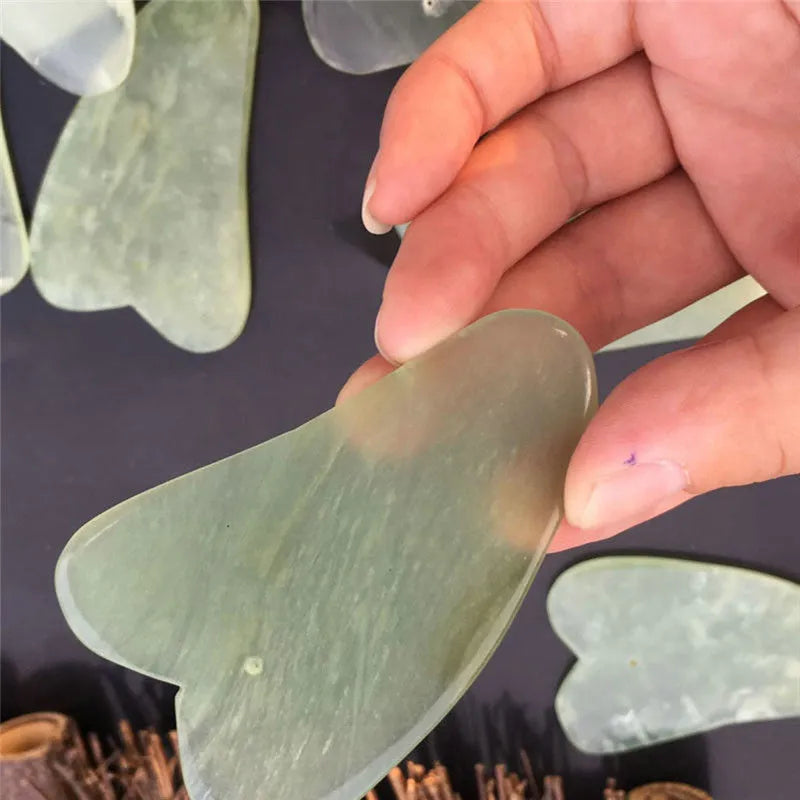 Natural jade gua sha scraper in heart shape on a light surface, 6.3cm x 4.5cm, hand-polished stone