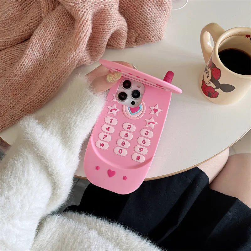 Pink silicone iPhone case shaped like a flip phone with a built-in mirror, showing cute cartoon style.