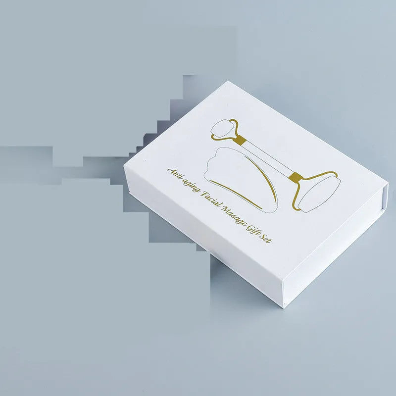Natural white jade double-headed facial roller and gua sha scraping board set on a plain background.