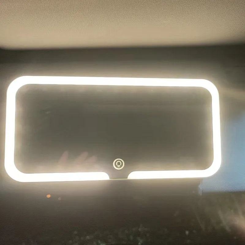 White car sun visor with LED make-up mirror showing illuminated reflection on aluminium surface