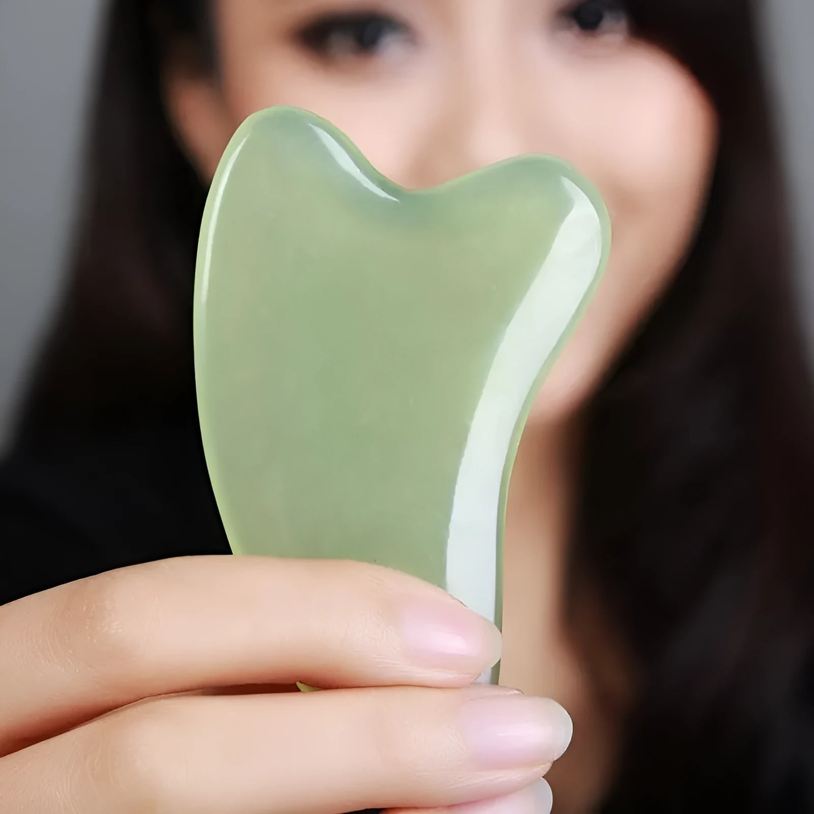 Natural jade gua sha scraper in heart shape on a light surface, 6.3cm x 4.5cm, hand-polished stone