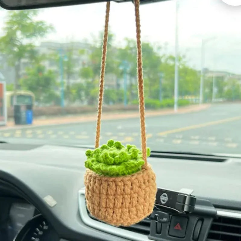Green and white knitted wool car plant decoration with macramé texture and a white hanging rope.