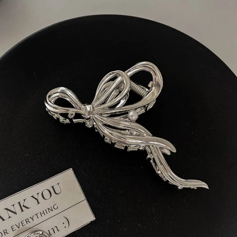 Assorted silver metal hair claws and barrettes including wave, knot, bow, and pearl designs on a white background.