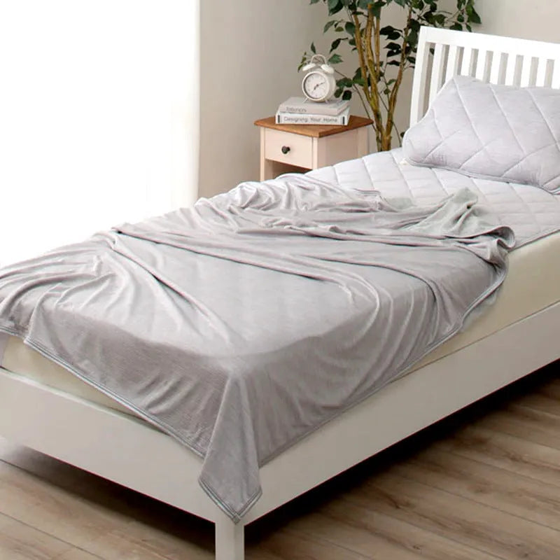 A blue polyester cooling blanket with Q-Max 0.4 technology laid on a bed.