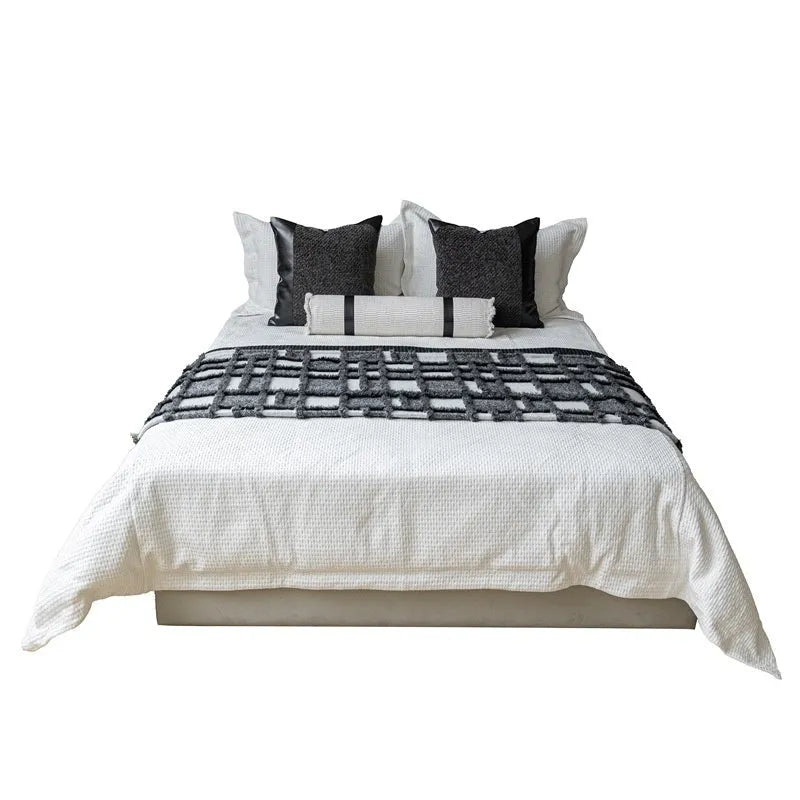 Modern minimalist grey and white plaid bed runner blanket with matching pillowcase and round pillow on a double bed.