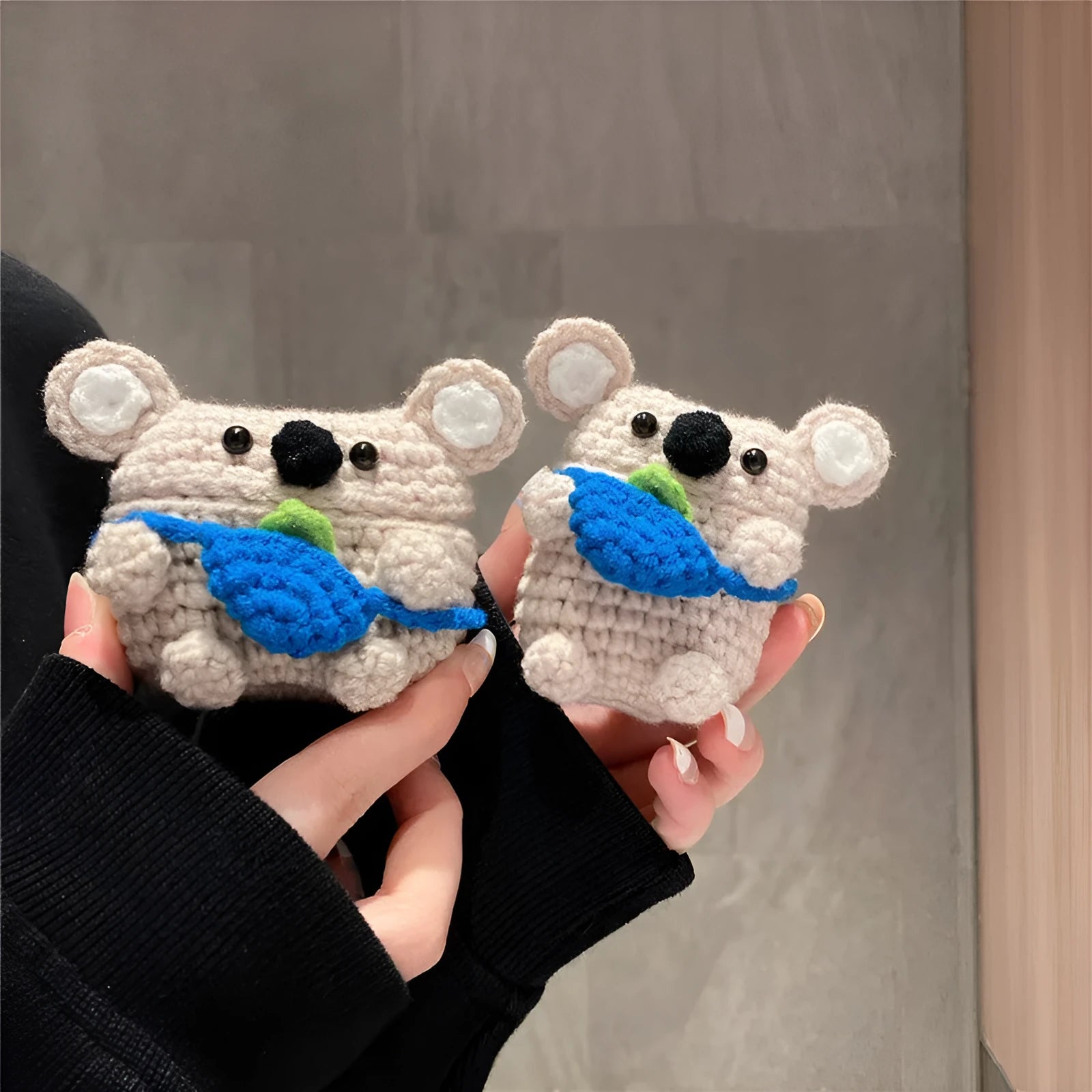 Handmade knitted koala bear backpack cover for Apple Airpods case on a table.