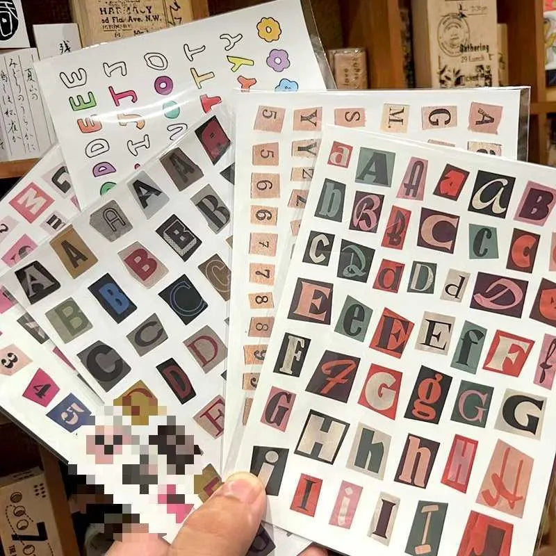 Set of printed cute-style stickers showing English letters A, B, C, D, E, numbers, symbols, and weekly words on a sheet.
