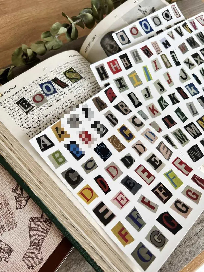 Set of printed cute-style stickers showing English letters A, B, C, D, E, numbers, symbols, and weekly words on a sheet.