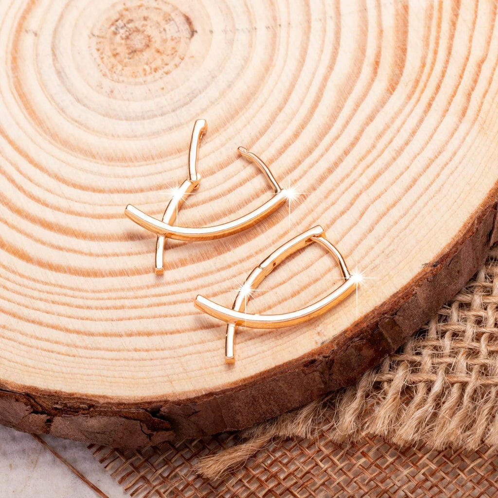 A pair of rose gold finished copper cross shaped drop earrings on a plain background.
