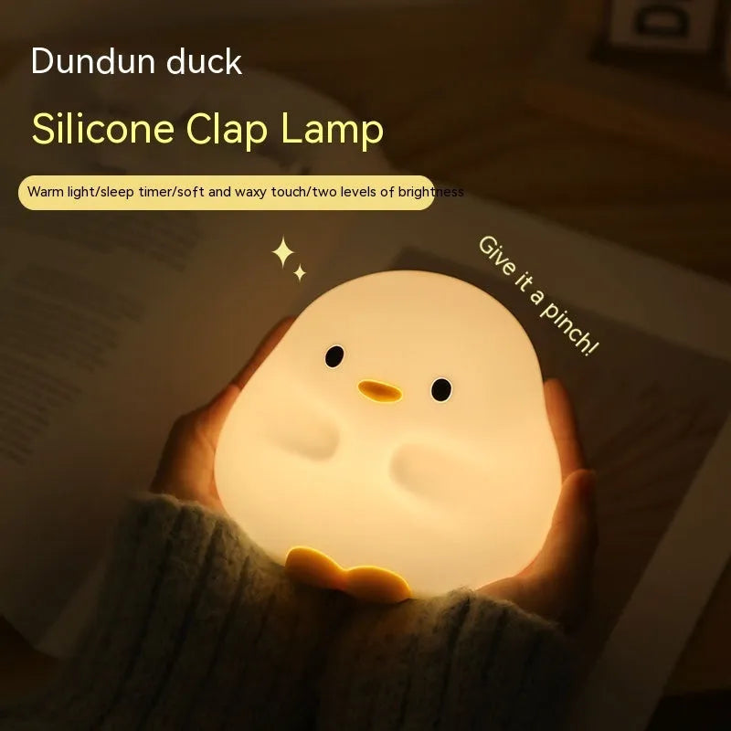 Cute duck-shaped silicone LED night lamp on a bedside table with warm light