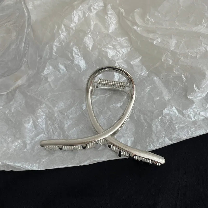 Assorted silver metal hair claws and barrettes including wave, knot, bow, and pearl designs on a white background.