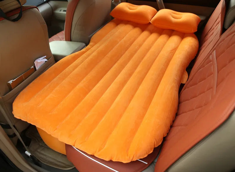 Black inflatable car bed with flocked surface set up in the back of a five-seater vehicle with pillows.