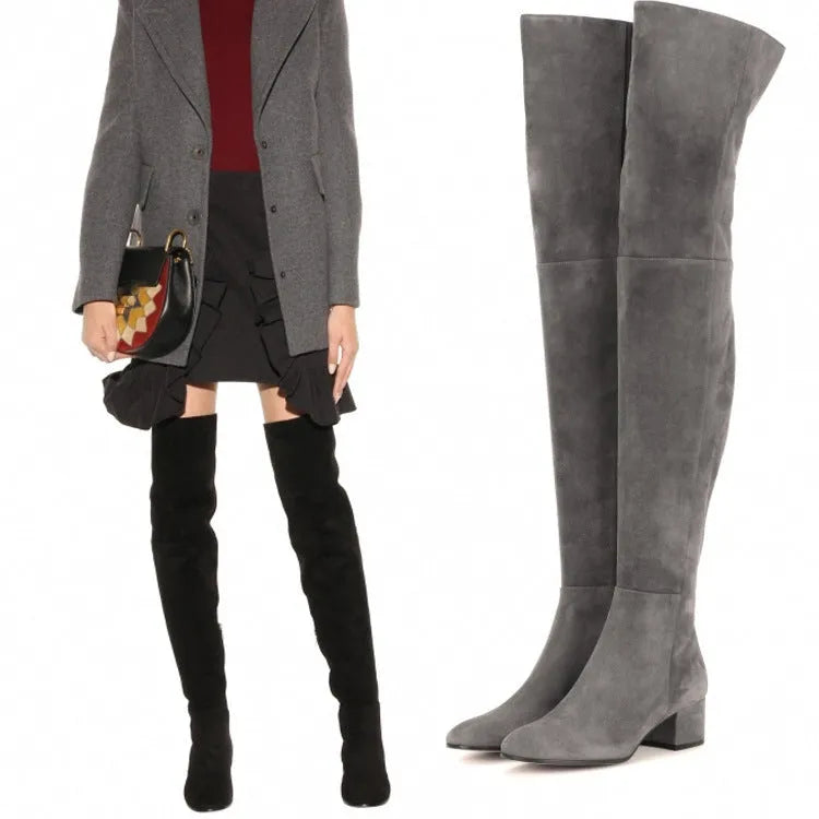 Women's grey suede over the knee flat boots with a low thick heel and pointed toe on a neutral background.