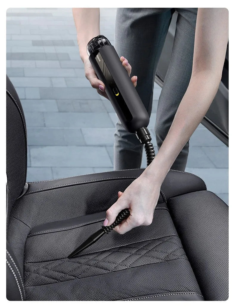 Black cordless handheld car vacuum cleaner with blowing hose attachment on a desktop.