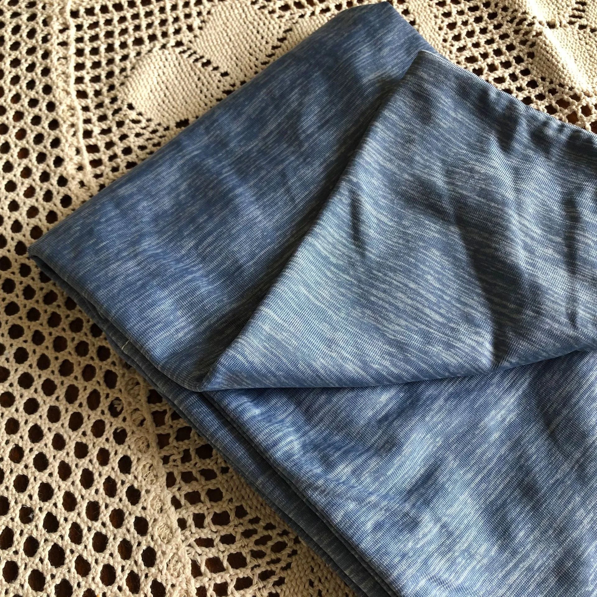 A blue polyester cooling blanket with Q-Max 0.4 technology laid on a bed.