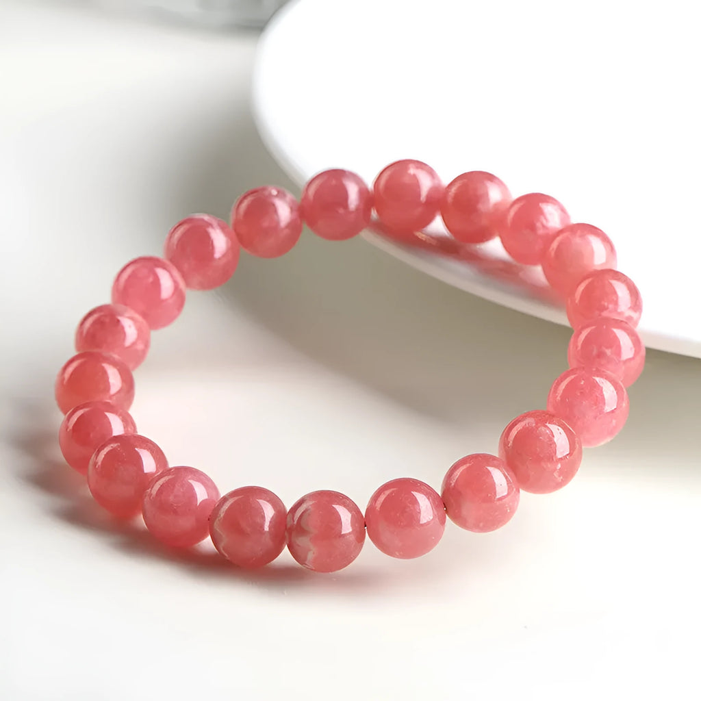 Women's geometric crystal bracelet with red rhodochrosite stone and a Longevity Lock charm on a wrist.