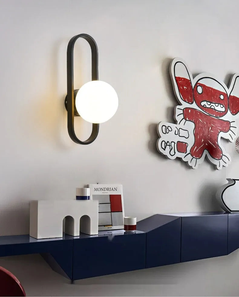 Minimalist modern wall lamp with a clear glass shade on an iron body, shown in a black finish mounted on a wall.