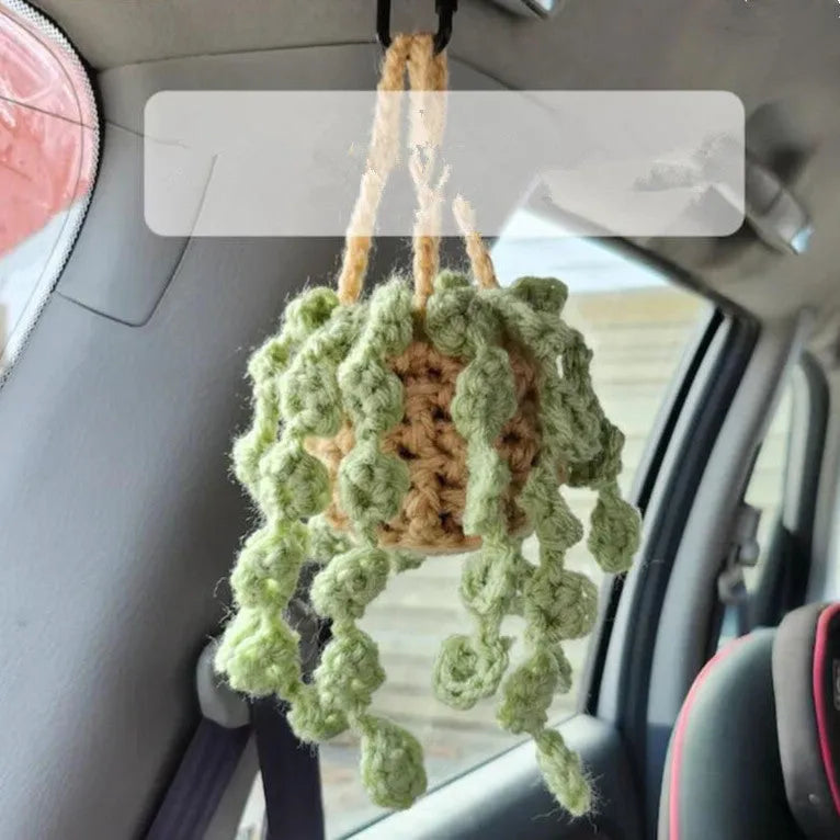 Green and white knitted wool car plant decoration with macramé texture and a white hanging rope.