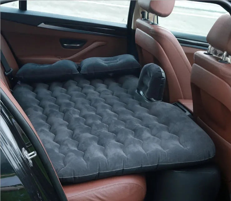 Black inflatable car bed with flocked surface set up in the back of a five-seater vehicle with pillows.