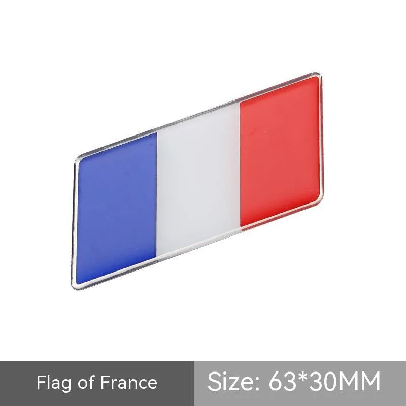 Aluminium parallelogram car sticker showing a national flag design, measuring 6.3 by 3 centimetres.