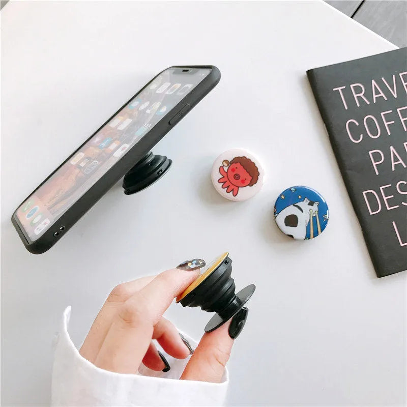 Creative telescopic glue cartoon phone airbag bracket in colour C1 girl design on a desk holding a smartphone